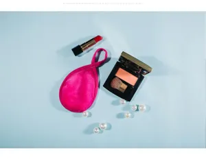 Dettaglio di un pugno struccante rosa a goccia con accessori di trucco su sfondo azzurro pulito.