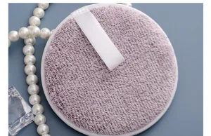 Suave borla de limpieza facial violeta redonda con asa de cinta blanca para desmaquillar.