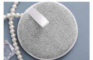 Detalle en primer plano de suave borla de limpieza facial de microfibra gris con cinta.