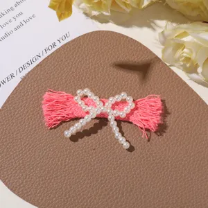 Detailed close-up of a DIY handmade pink tassel hair clip decorated with white pearls.