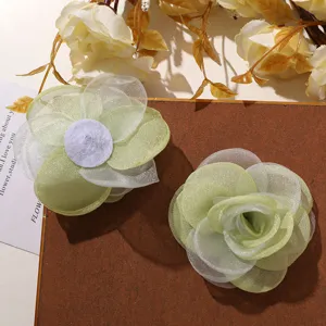 Vista detallada de accesorios de flores de organza verde hechos a mano, pinza de pelo y decoración.