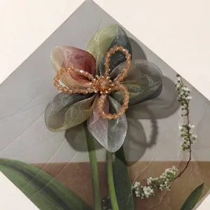 Detail shot of handcrafted gradient organza five petal flower with crystal bead center for hair accessories.