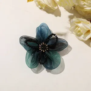 Close-up detail of blue and green gradient organza flower hair accessory with crystal bead center.