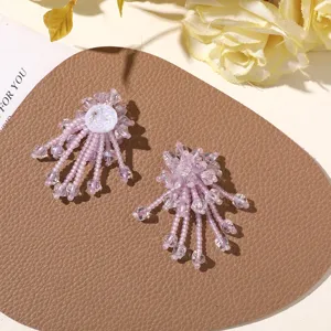 Detalle en primer plano de pendientes DIY de flores con flecos de cuentas violetas, estilo dulce.