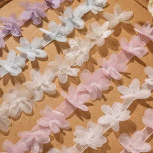 Dettaglio in primo piano di nastri con fiori in organza 3D perlati pastello, ideali per fai da te.