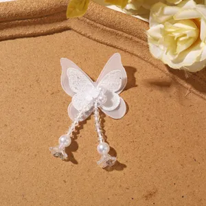 Close-up detail of white layered mesh butterfly patch with beaded tassel and faux pearls.