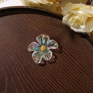 Detailed close-up of clear iridescent acrylic flower DIY charm with gold core on dark wooden tray.
