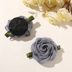 Close-up detail view of grey fabric rose flower accessory with green leaves and black backing.