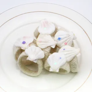 Primo piano dettagliato di portatovaglioli in conchiglie naturali su un piatto di ceramica bianca.