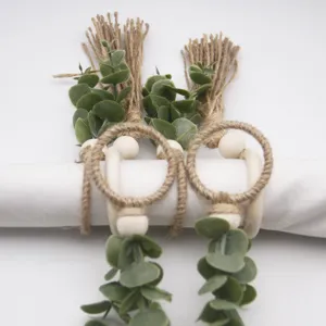 Handmade jute rope napkin rings with wooden beads and faux eucalyptus leaves for rustic decor.