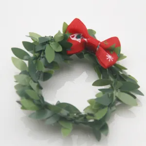 Nahaufnahme eines Weihnachts-Serviettenrings mit grünen künstlichen Blättern und roter Schleife.