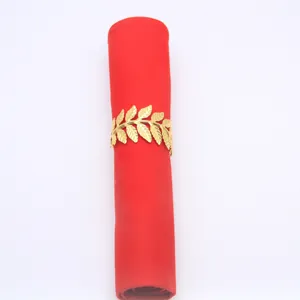 Detail view of a golden metal leaf napkin ring clasping a red table napkin for decoration.