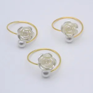 Elegant gold napkin rings featuring a white rose and pearl, perfect for dining table decor.