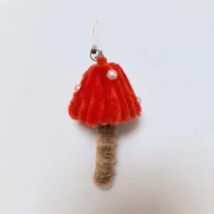 Dettaglio ciondolo fungo in scovolino fatto a mano, cappello rosso con perle e gancio metallico.