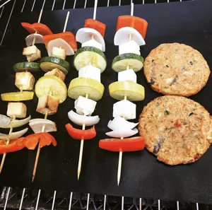 Gedetailleerd overzicht van teflon grillmat met groentespiezen en hamburgers erop.