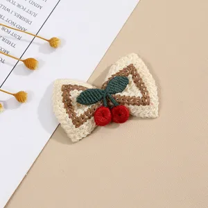 Detailed view of cute knitted embroidered cherry bow hair clip and clothing patch accessory.