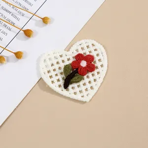 Close-up of white crochet heart patch with red flower embroidery on clean textured background.