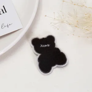 Detailed shot of brown teddy bear plush patch with embroidered lettering for DIY garment decor.