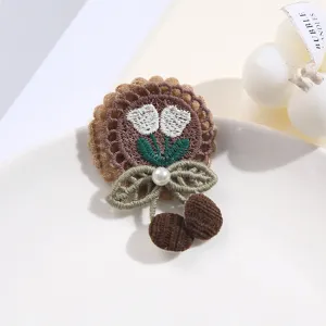 Detailed shot of a cute lace embroidered tulip patch with pearls and pom-poms on a white plate.
