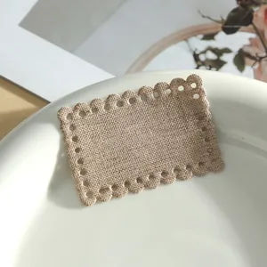 Close-up detail of beige linen fabric patch with scalloped edge and hollow holes for DIY decor.