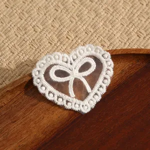 Close-up of white heart lace bow embroidery patch, delicate DIY clothing accessory.