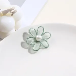 Close-up detail of green lace flower patch with central pearl, ideal for DIY clothing decoration.