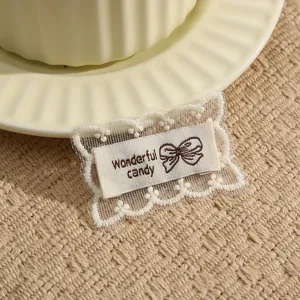 Close-up detail of lace embroidered patch with bow design and cute letter typography for DIY craft.