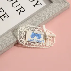 Close-up of white lace patch with blue bow embroidery and pearl pendant detail accessory.