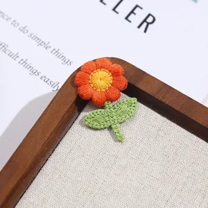 Close up of cute orange flower embroidery patch with green leaves, detailed stitching for clothes.