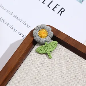Close-up detail of grey embroidered daisy patch with yellow center and green leaves on board.