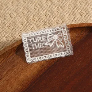 Close-up detail of white lace embroidered patch with bow design for DIY garment decoration.