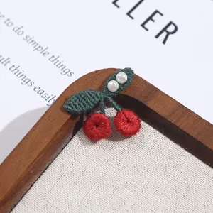 Detailed close-up view of a cute embroidered cherry fabric patch with white pearl beads.