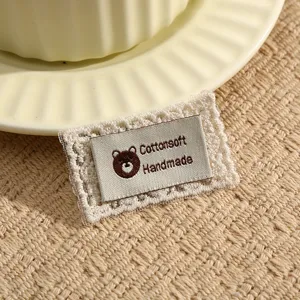 Detailed shot of a cute bear fabric label embroidery patch with lace border for DIY sewing crafts.