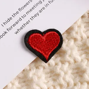 Gros plan d'un charmant patch brodé en forme de cœur rouge et noir sur un tissu tricoté.