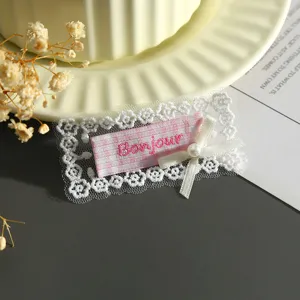 Close-up of pink checkered lace patch with Bonjour embroidery and cute pearl bow detail.