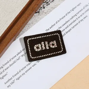 Detailansicht eines bestickten Buchstaben-Aufnähers, brauner Stoff mit weißer Stickerei.