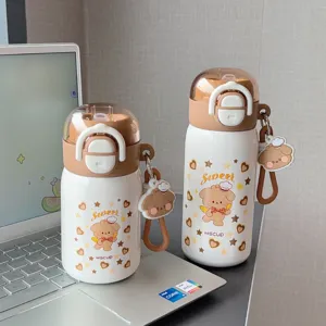 Close-up detail of cute cartoon bear insulated water bottles with straw and hanging charm on desk.