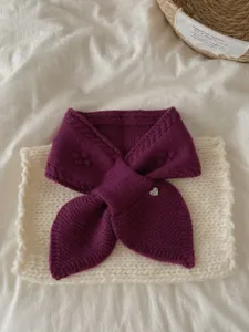 Detail shot of cozy purple knitted winter short scarf with cute heart charm on white mat.