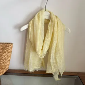 Light yellow crinkled scarf detail showing soft textured fabric and delicate fringe edge.