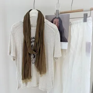 Detail view of the crinkled solid color long scarf draped on a casual clothing display setup.