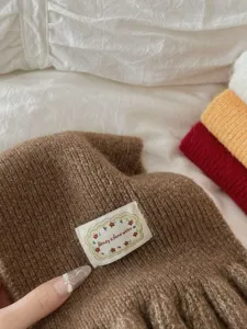Knitted scarf detail shot showing soft brown fabric texture and cute embroidered label accent.