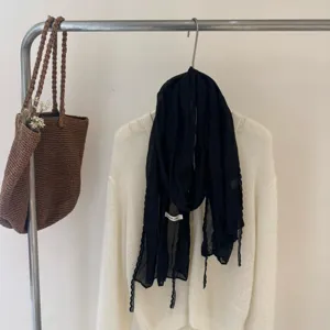 Close-up detail view of a lightweight black thin silk scarf draped on a white cardigan rack.