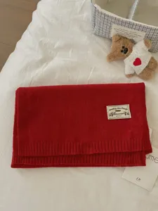 Red knit scarf detail close-up, soft woolen fabric texture with brand label and cute bear prop.