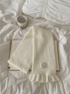 Cozy white knitted scarf for women, featuring a chic ruffle hem and stylish decorative label.
