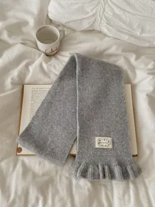 Grey knitted scarf with elegant ruffle trim and cozy texture, detailed shot of winter accessory.