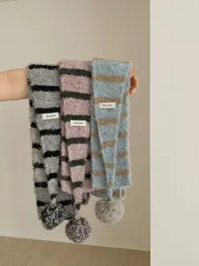 Close-up detail of cozy striped fuzzy winter scarf with cute pom-pom and stitched woven label.