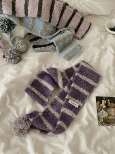 Detail view of cozy winter knitted striped scarf with pom-pom and tag, soft textured fabric.