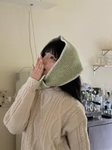 Close-up detail shot of a stylish green knitted hooded scarf in a cozy cafe setting.