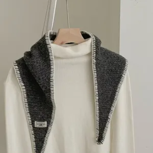 Grey knitted scarf with white contrast stitch edge and small brand label, elegant winter accessory.
