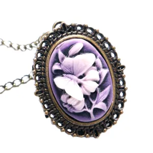 Gedetailleerde close-up van vintage brons cameo ketting met paarse vlinder en bloemmotief.